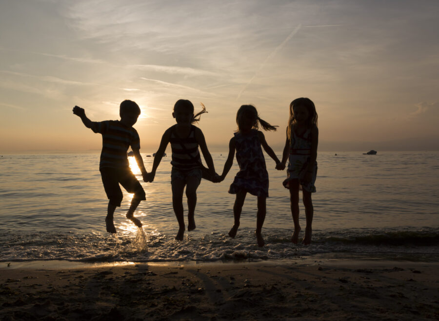 Italy, Lake Garda, children jumping on beach at sunset